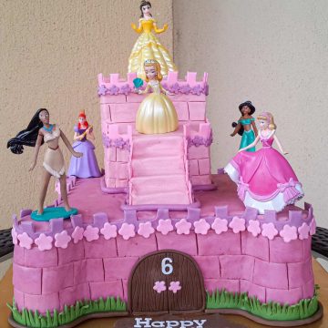 A two tier castle cake in pink, decorated with 6 Disney princess toy toppers.