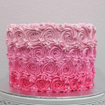 A round cake decorated with pink buttercream rosettes