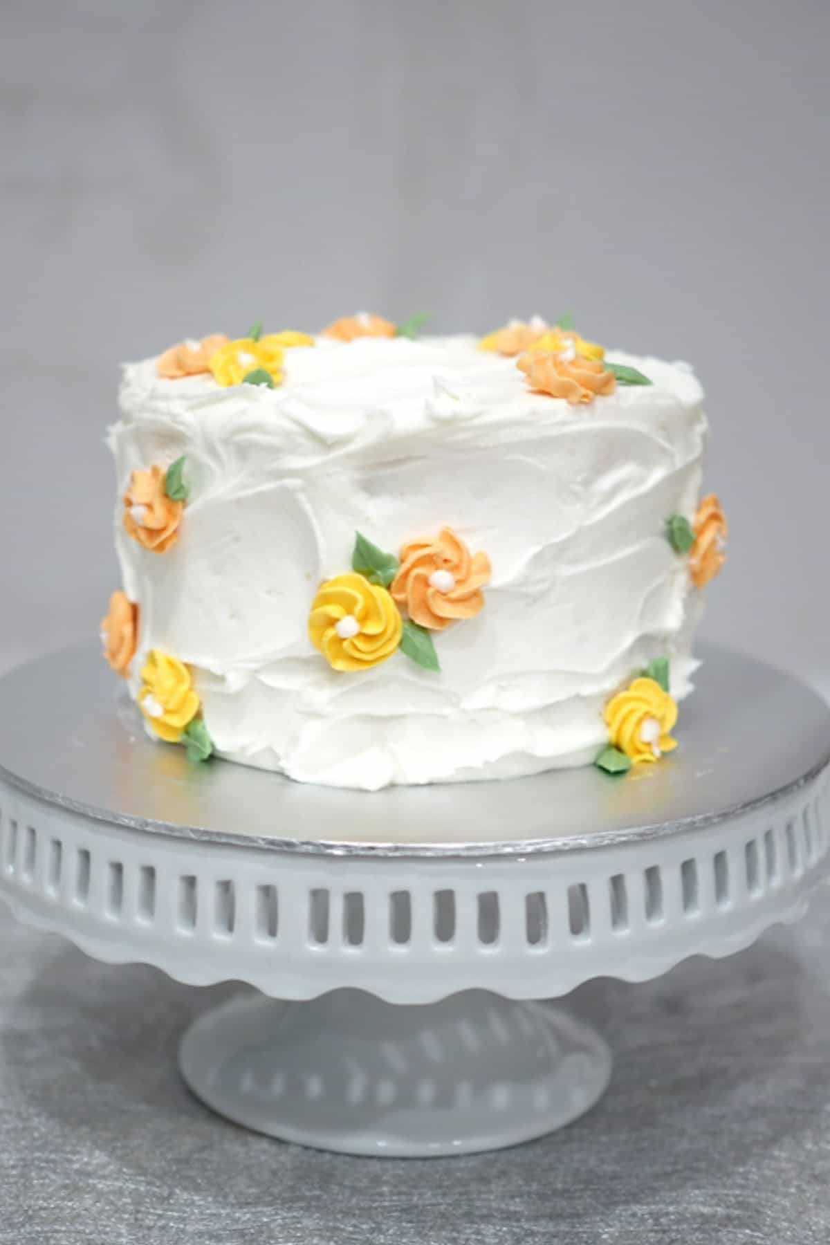 A round cake decorated with white buttercream and orange and yellow piped buttercream flowers. 