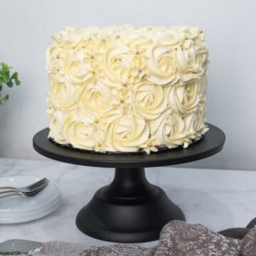 A round cake covered in buttercream frosting rosettes in white, on a black cake stand.