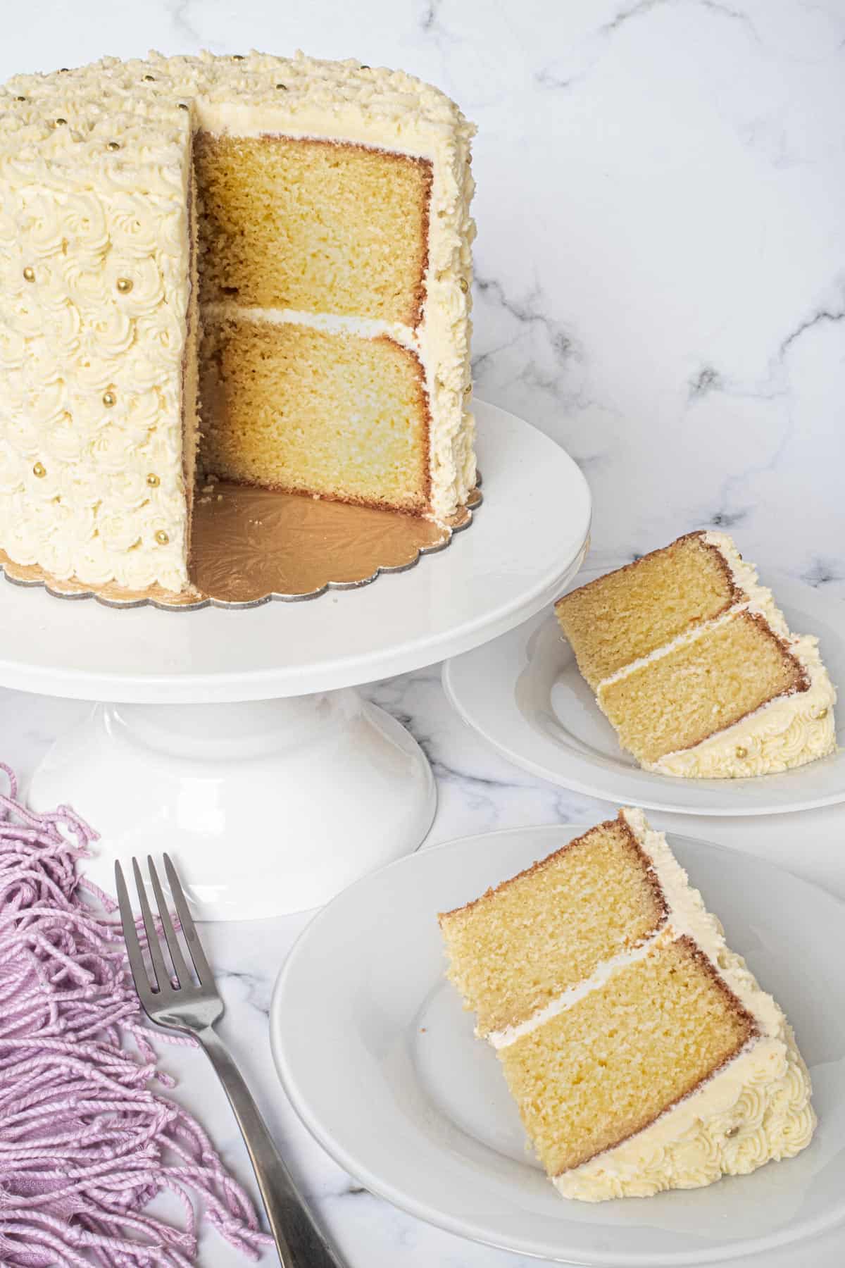 A round old school butter pound cake covered in buttercream on a white cake stand. A slice of the cake is cut out.