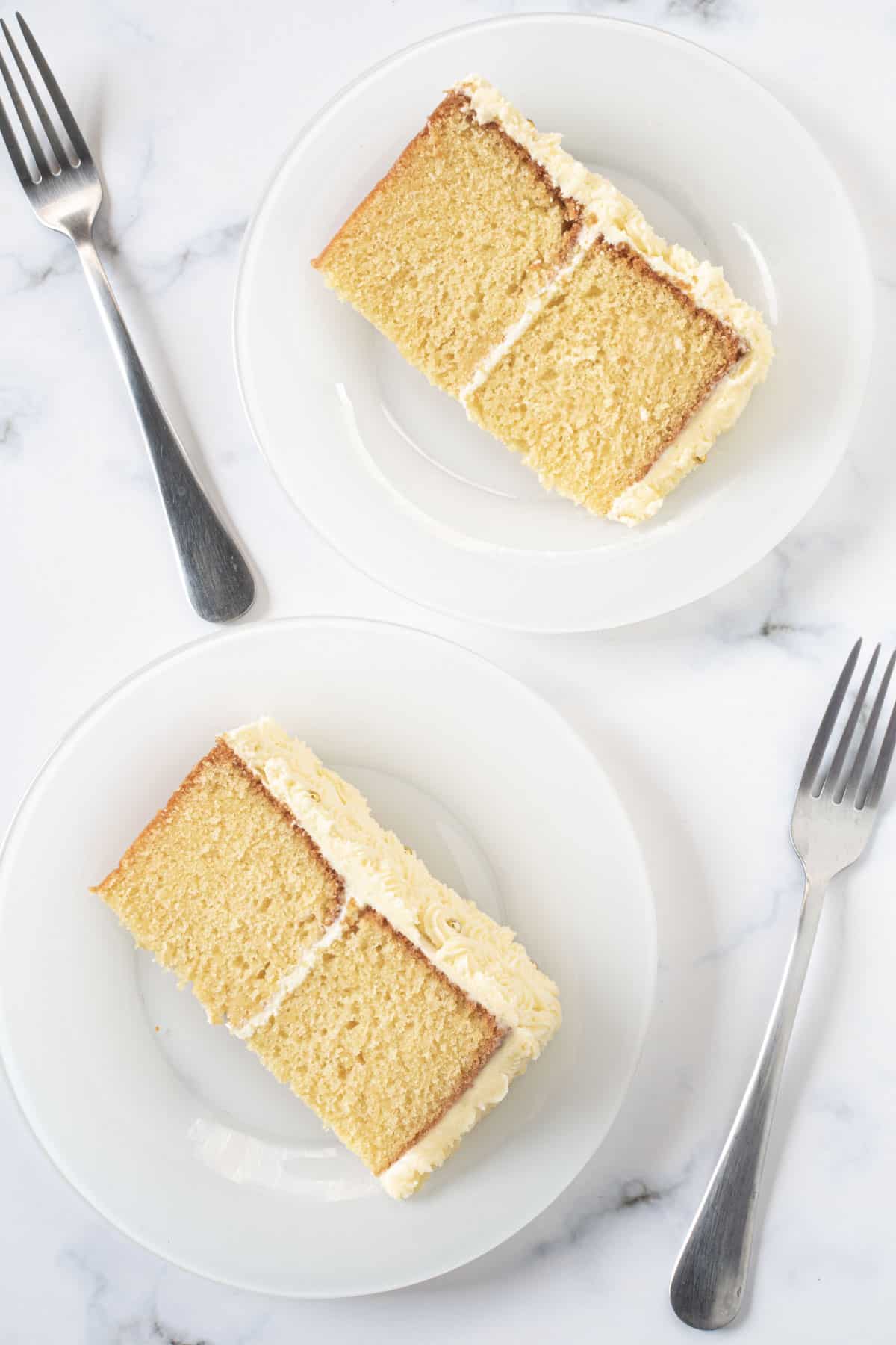 Two slices of white cake on a white plates. Cakes consist of 2 layers sandwiched and covered in buttercream.