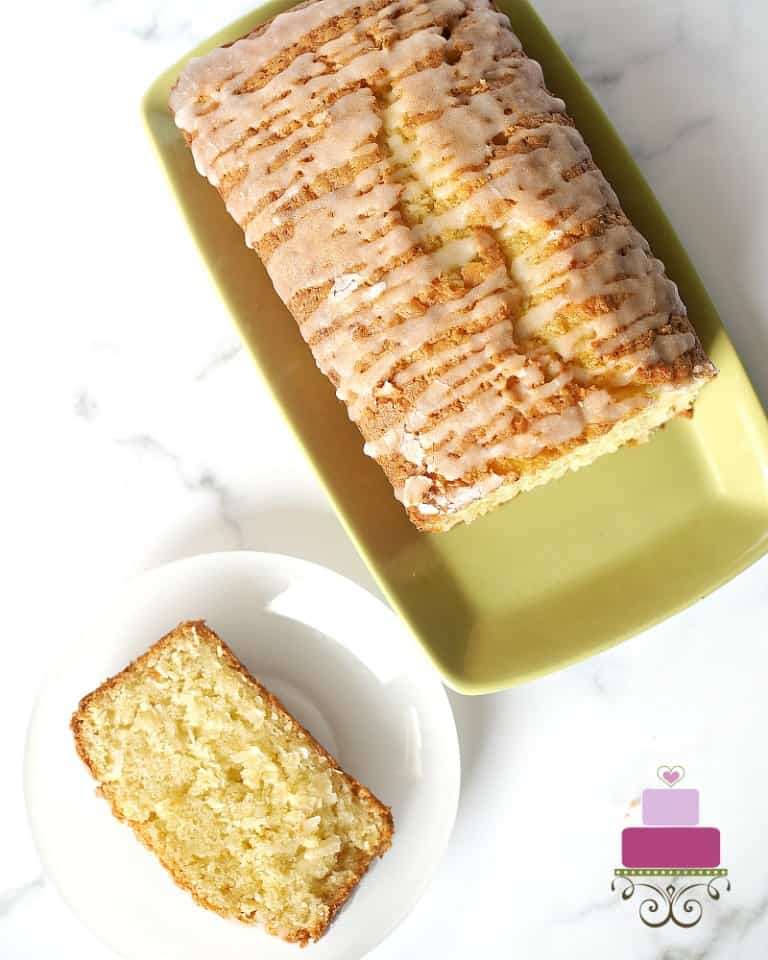 A loaf cake glazed with sugar icing, with a slice cut onto a white plate