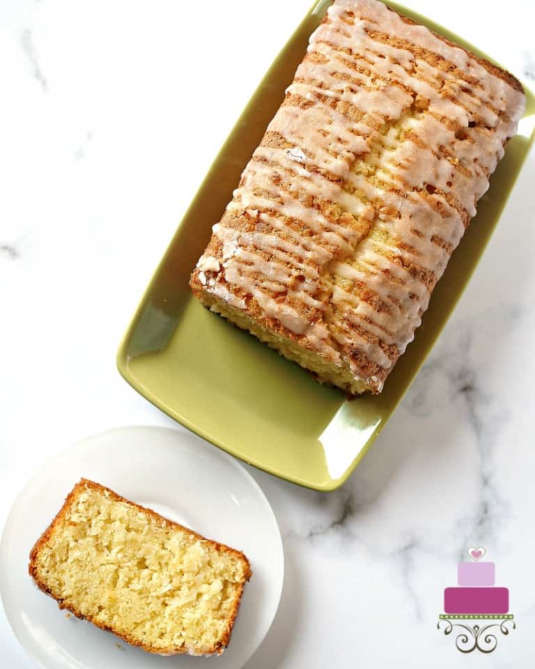 A loaf cake glazed with sugar icing, with a slice cut onto a white plate