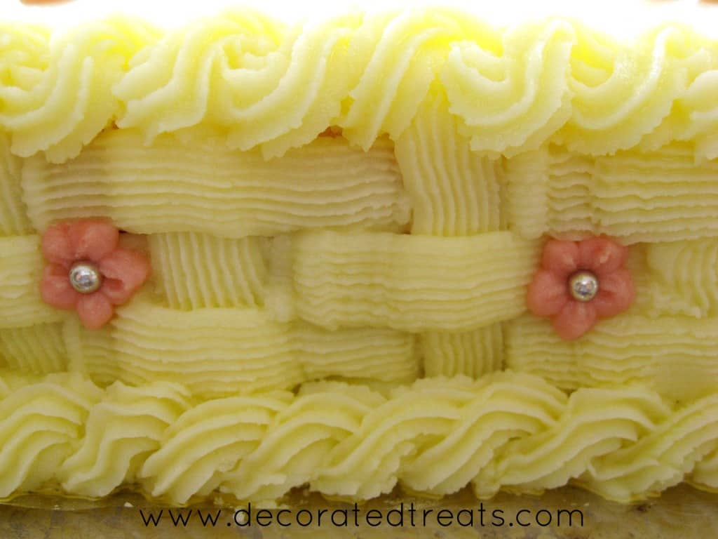 Buttercream basket weave piping on the side of a cake, with pink piped flowers