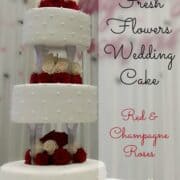 3 tier wedding cake on pillars, decorated with fresh red and champagne colored roses
