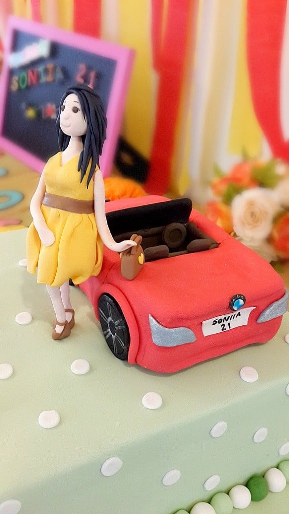 A square green polka dots cake with a stylist lady figurine and a BMW car cake topper.