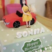 A square green polka dots cake with a stylist lady figurine and a BMW car cake topper.