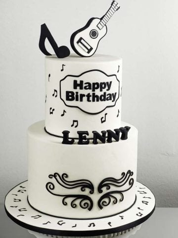 A black and white 2 tier cake with guitar topper and black music note topper