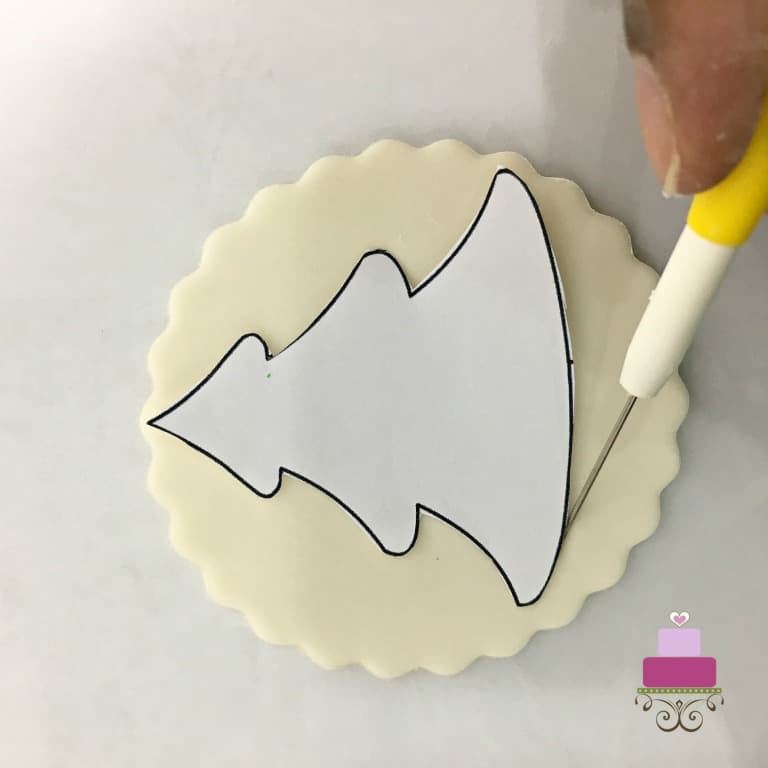 Tracing the image of a Christmas tree with a needle tool, onto a round piece of fondant