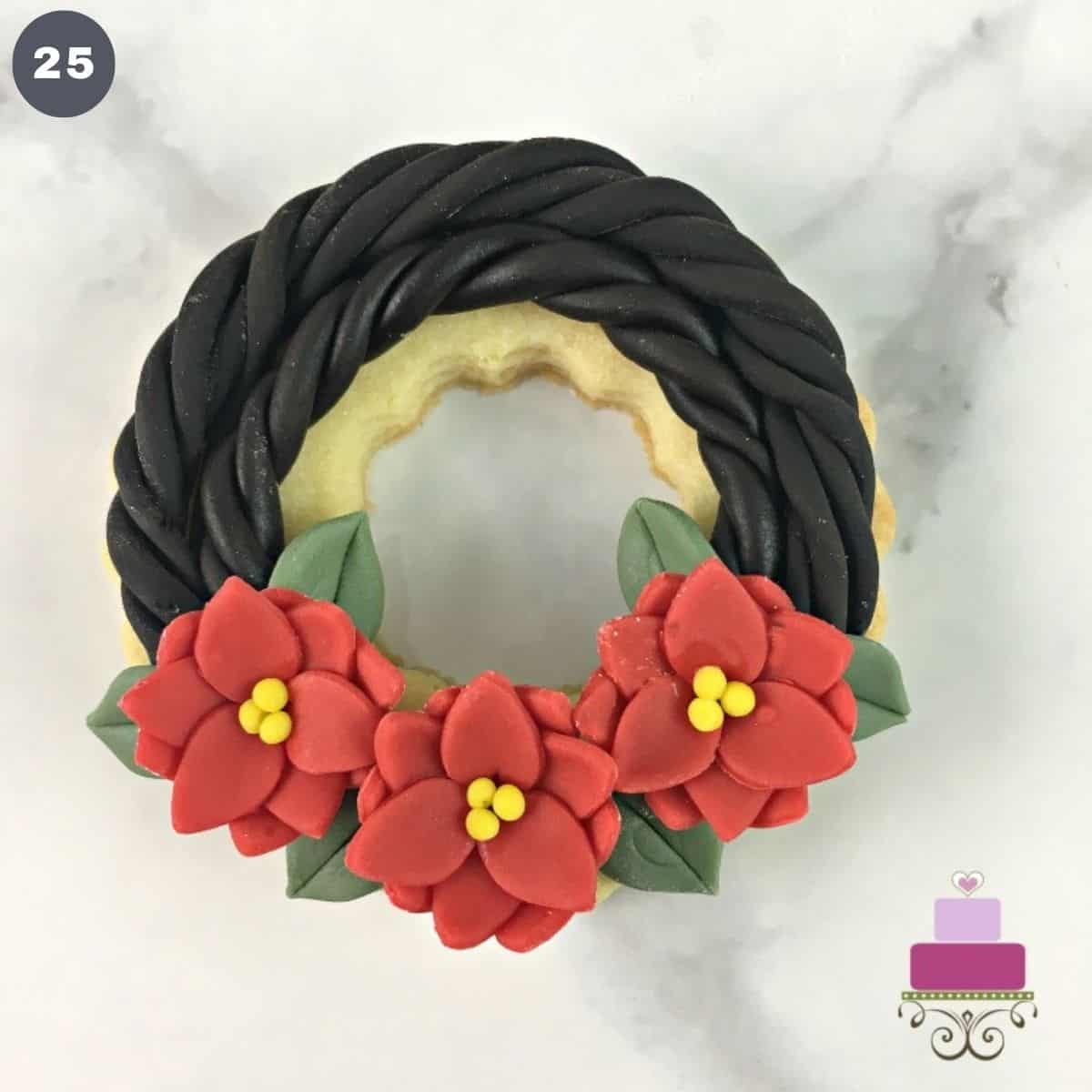 A ring shaped cookie decorated into a wreath with poinsettia flowers.