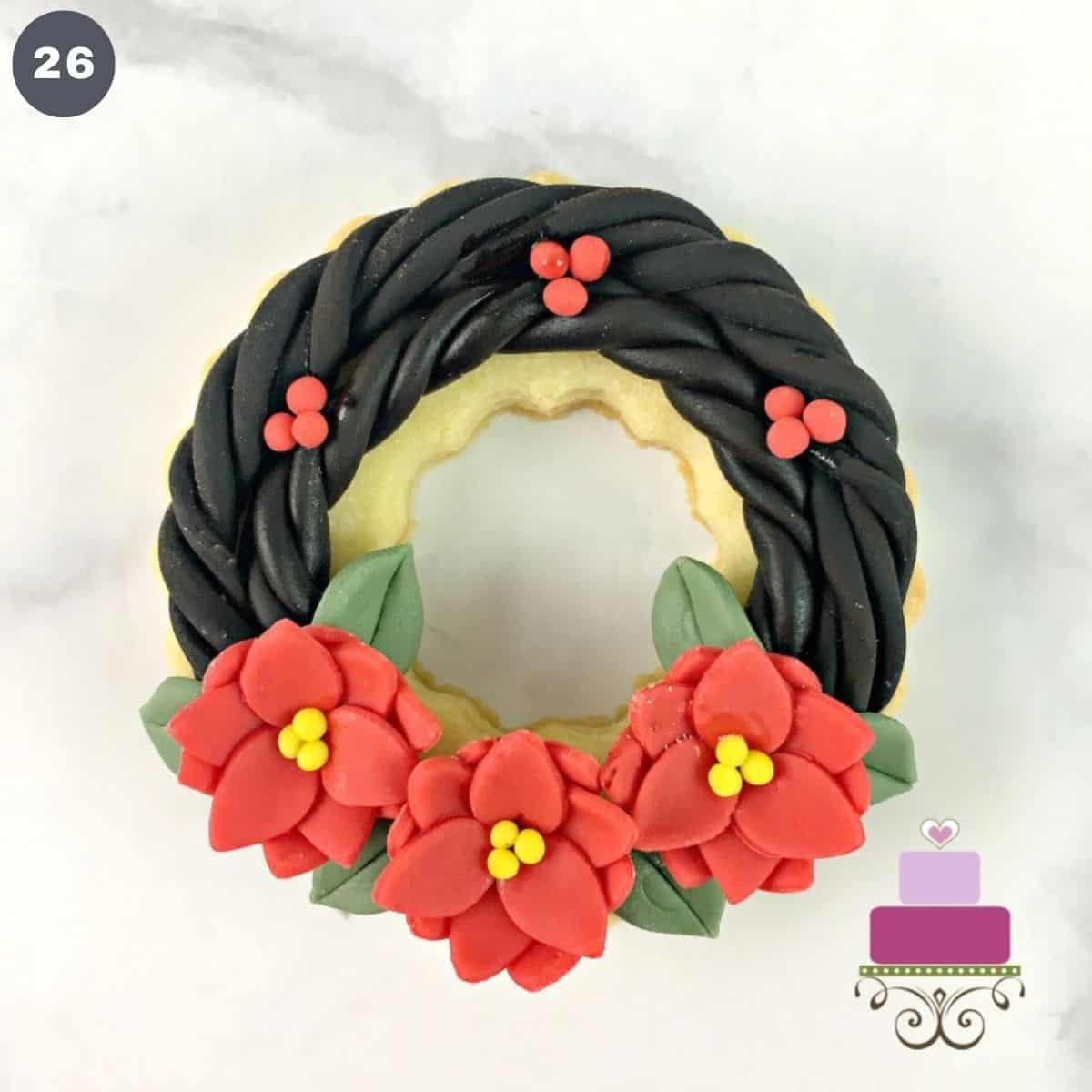 A ring shaped cookie decorated into a wreath with poinsettia flowers and holly berries.