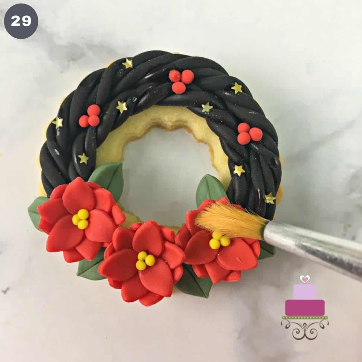 Using a brush to brush to top of a fondant decorated cookie.