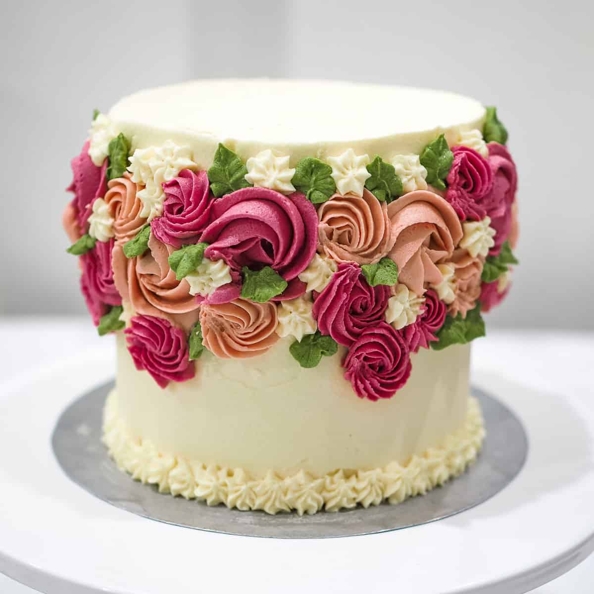 A round rosette cake in white, pink, burgundy and green.