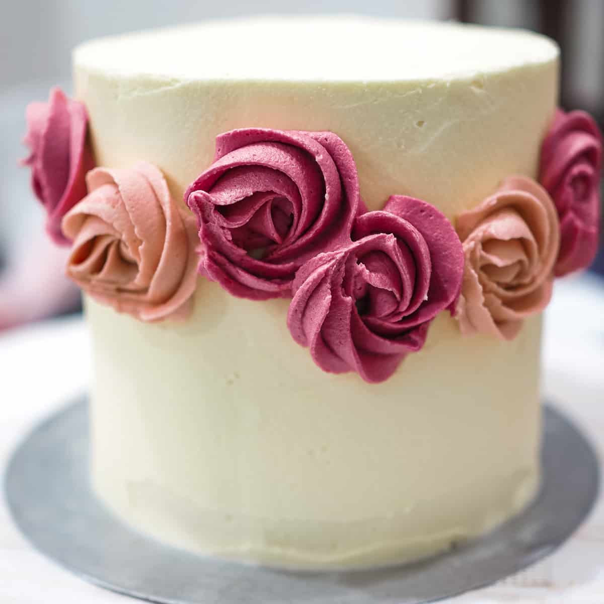 Buttercream rosettes in burgundy and pink on the sides of a round buttercream cake