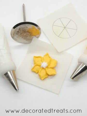 2 piping bags filled with white and yellow royal icing, with a flower nail and a pipe yellow flower in between