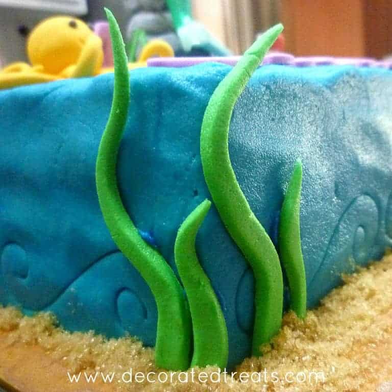 The corners of a square cake decorated in butter icing and fondant leaves.