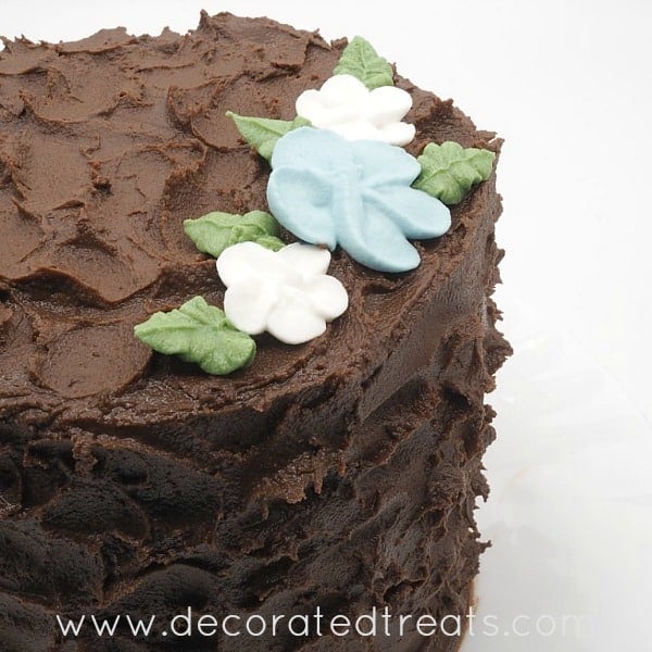 A round chocolate cake covered in chocolate icing and decorated with royal icing flowers