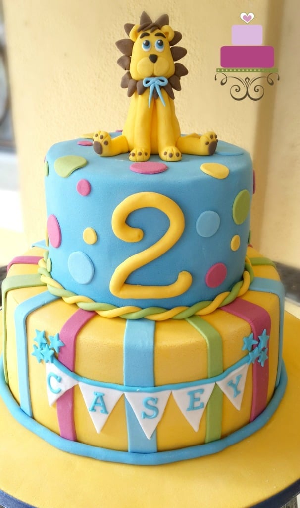 A two tier cake in yellow and blue with a lion cake topper and a large number 2 on the top tier.