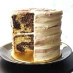 A round marble cake covered in marbled buttercream. A slice of the cake is cut out.