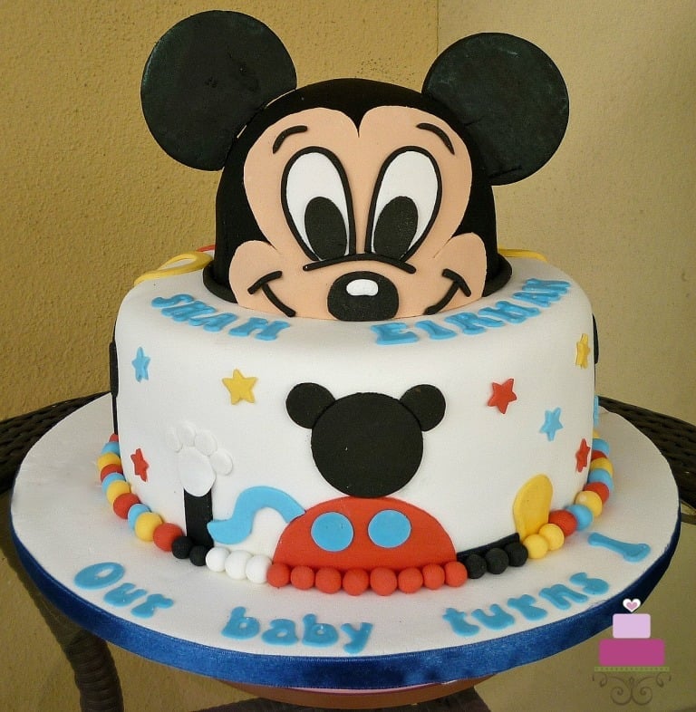 A round cake with 3D Mickey face as the top tier, decorated in Mickey Mouse clubhouse theme.