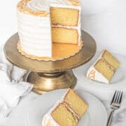 A round cake decorated with candied orange peels. 2 slices are cut out onto white plates.