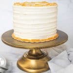 A round cake covered in white buttercream on a gold cake stand.