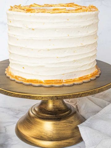 A round cake covered in white buttercream on a gold cake stand