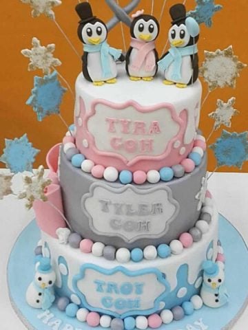A 3 tier cake in blue, silver and pink and 3 cute penguins toppers.