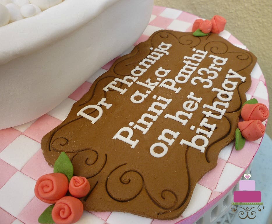 A brown fondant plaque with birthday message, on a pink and white checkered cake board.