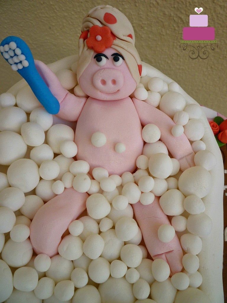 A pink 3D fondant pig in a lying position holding a blue brush