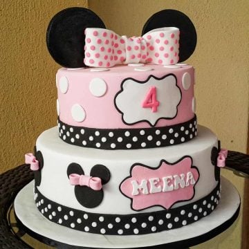 A 2 tier pink Minnie Mouse themed birthday cake with a large pink polka dots topper