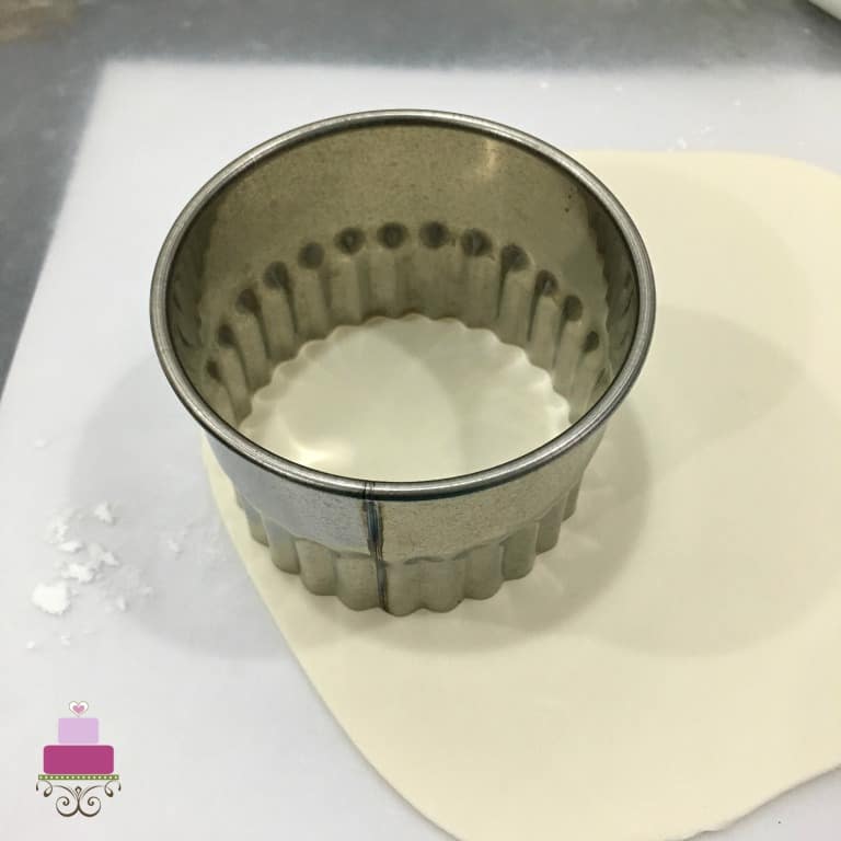 A scalloped round cutter on a piece of rolled white fondant