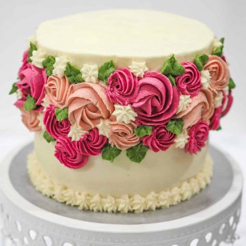 A round rosette cake in white, pink, burgundy and green.