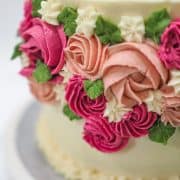 Close up of rosette buttercream flowers in burgundy and pink on the side of a cake.