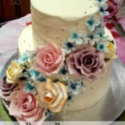 A two tier wedding cake with rustic buttercream deco, pink, purple and yellow roses and blue hydrangeas