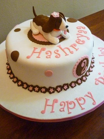 A round white cake with a brown and white fondant dog topper