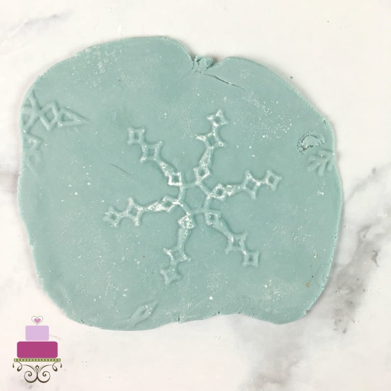 A snowflake pattern imprinted on a piece of blue fondant.
