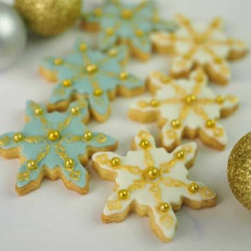 Sugar cookies in the shape of snowflakes decorated in blue, white and gold