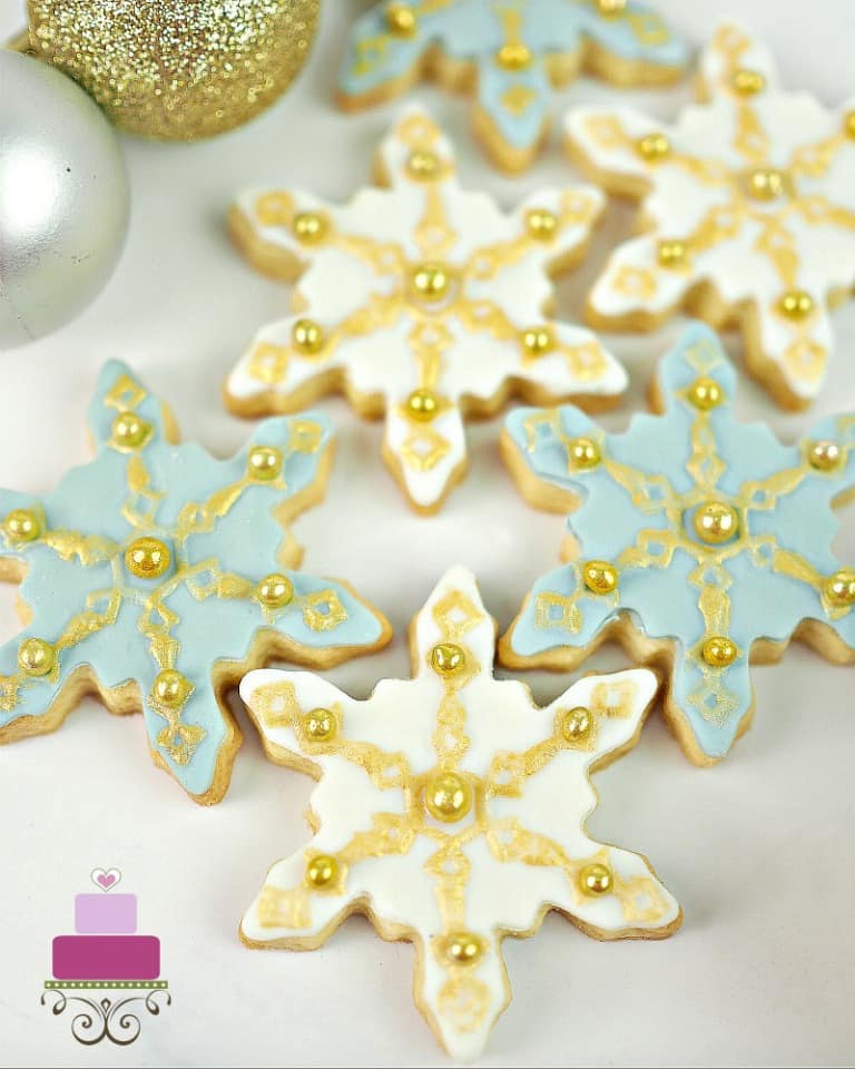 Sugar cookies in the shape of snowflakes decorated in blue, white and gold.