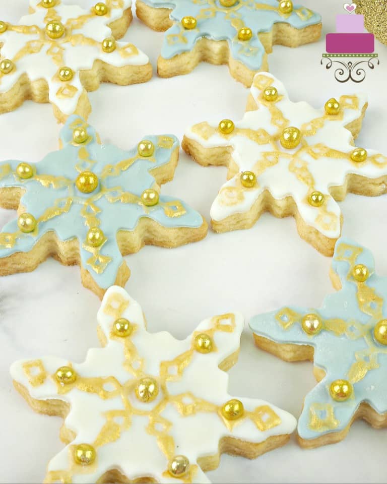 Sugar cookies in the shape of snowflakes decorated in blue, white and gold