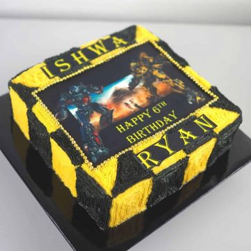 A square cake decorated with yellow and black buttercream squares and Transformers edible image.