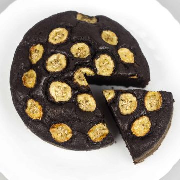 A round chocolate cake topped with caramelized banana slices. A slice of the cake is cut out