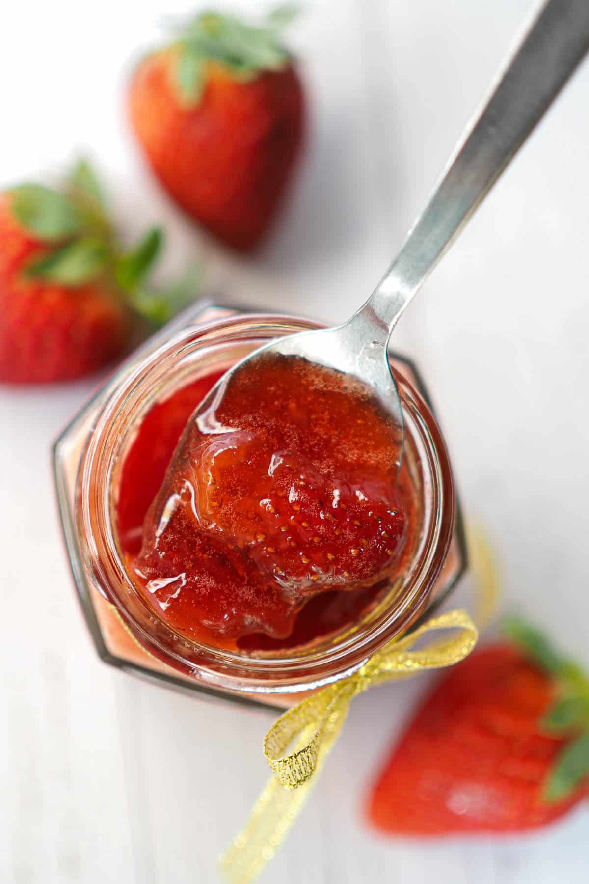 Top view of a jar of strawberry filling. A spoon is on top, filled with the filling