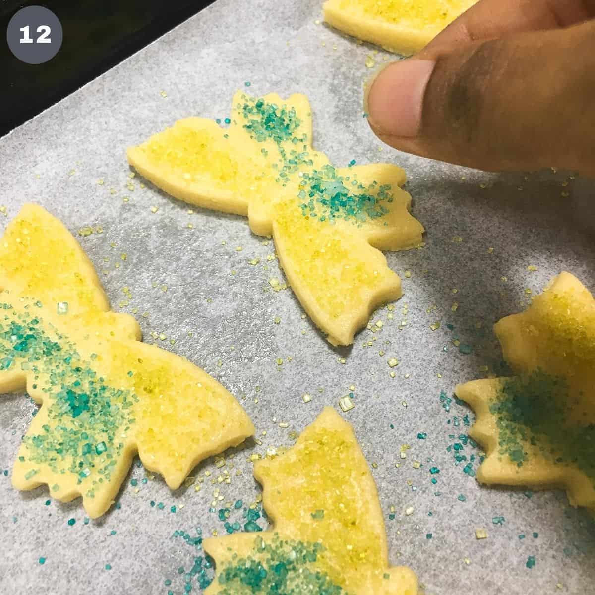 Sprinkling colored sugar on butterfly shaped cookies on a tray.