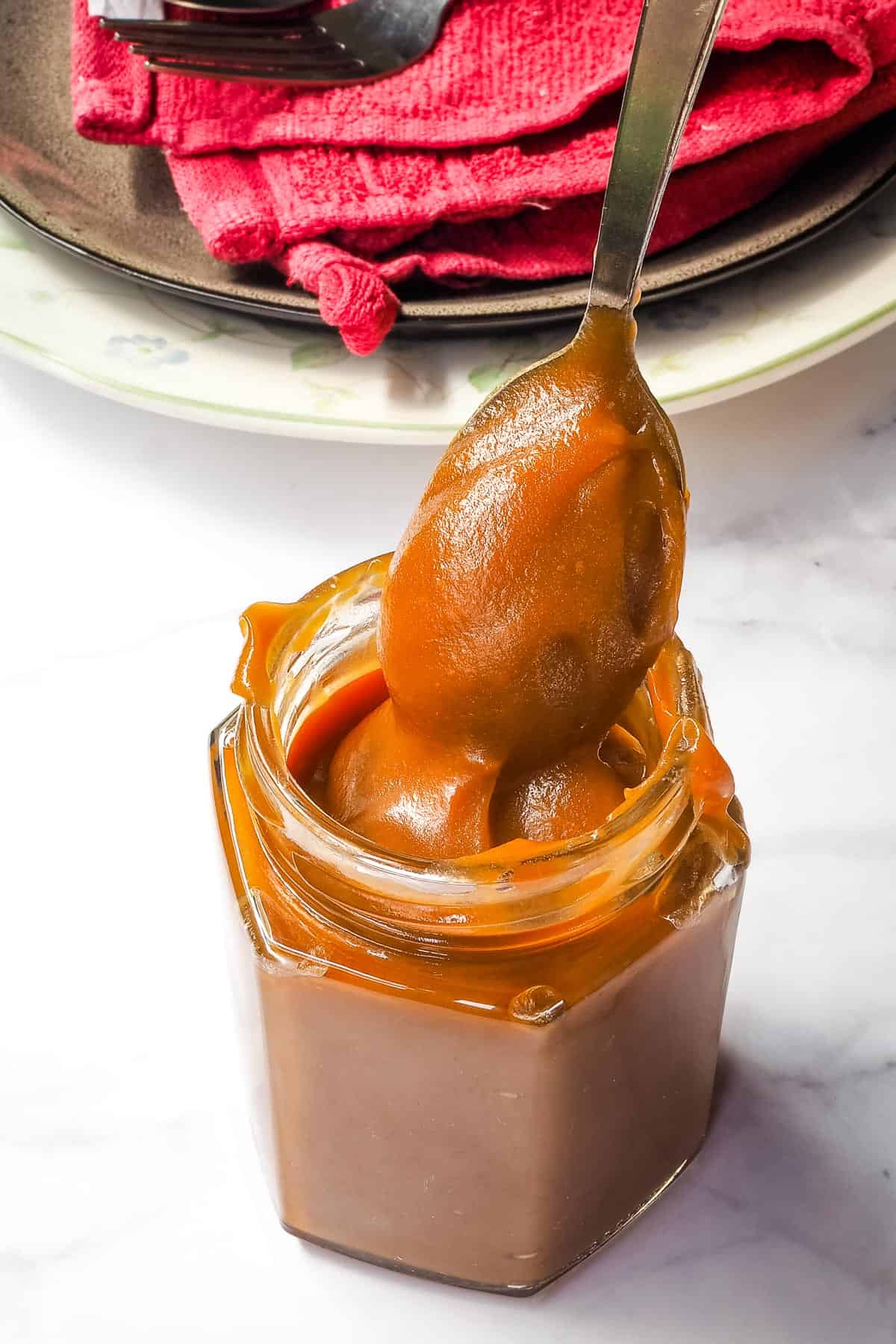 A spoon of salted caramel lifted up from a glass jar