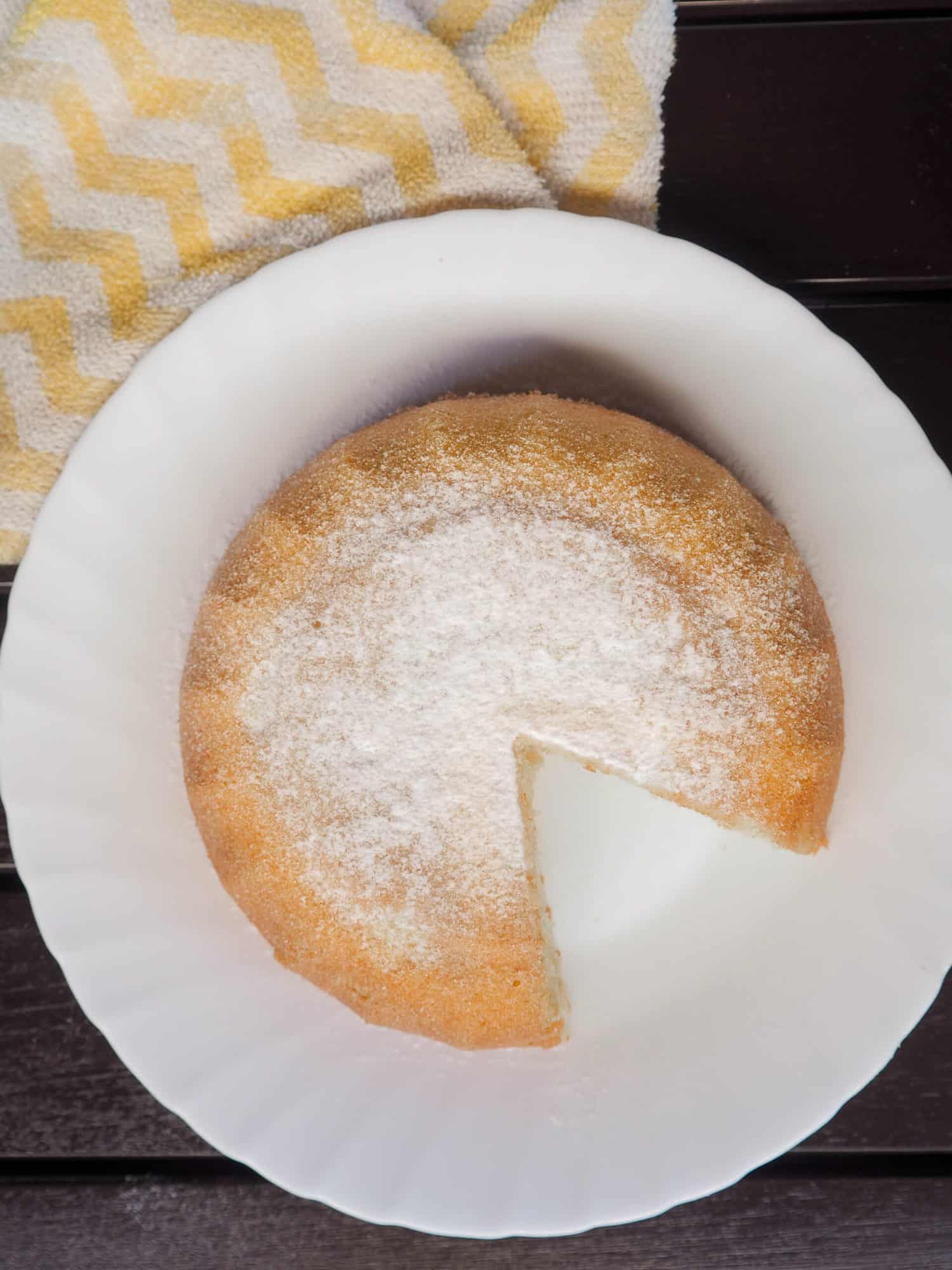 Top view of a bowl shaped cake with powdered sugar topping. A slice of the cake is cut out