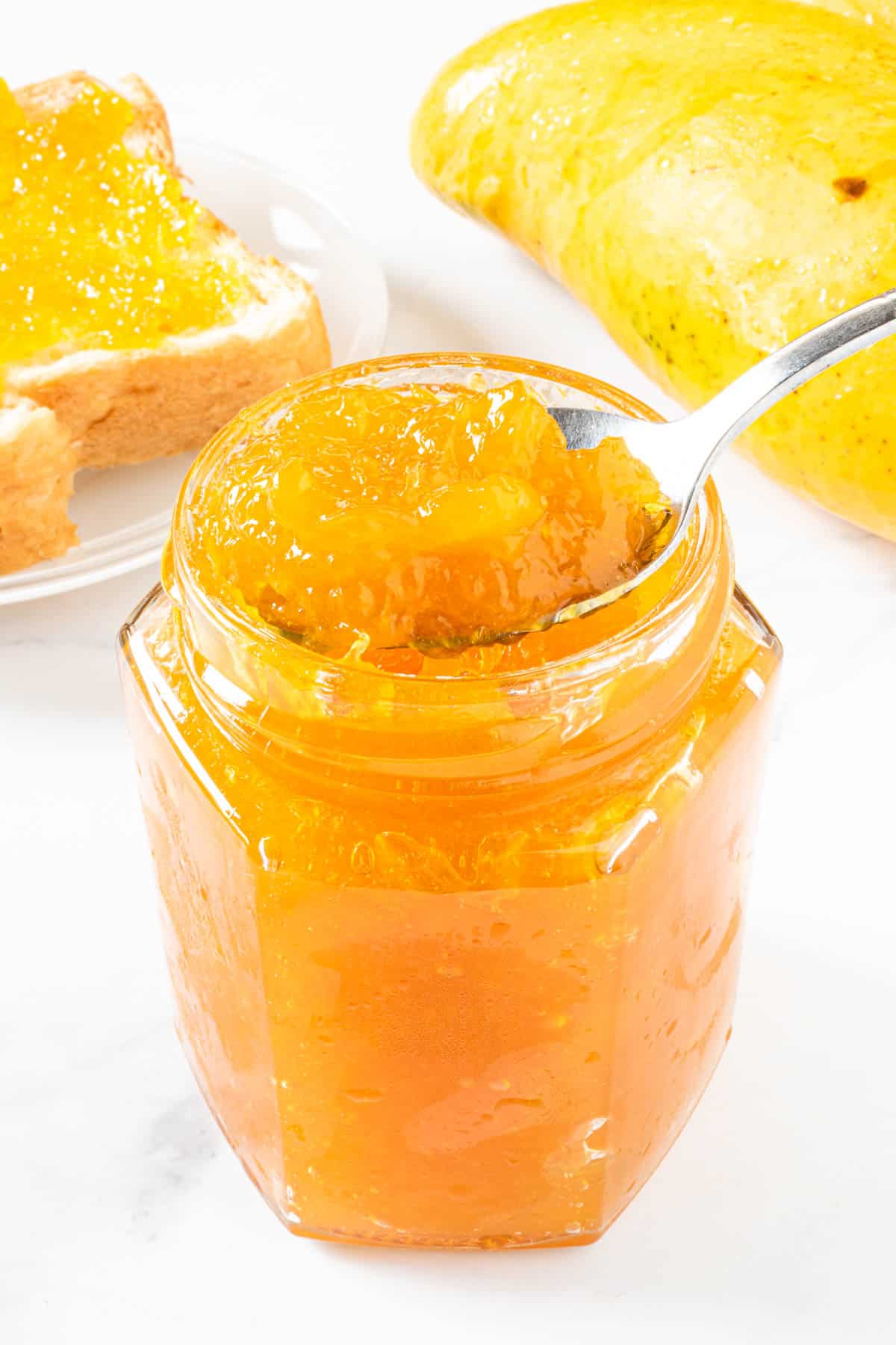 A spoon of yellow jam scooped out of a glass jar