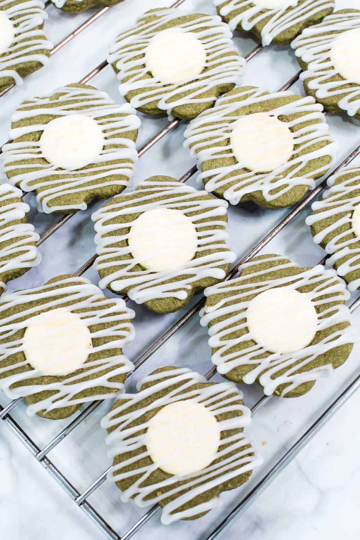 Green flower shaped cookies with white centers and icing drizzle, arranged on a wire rack
