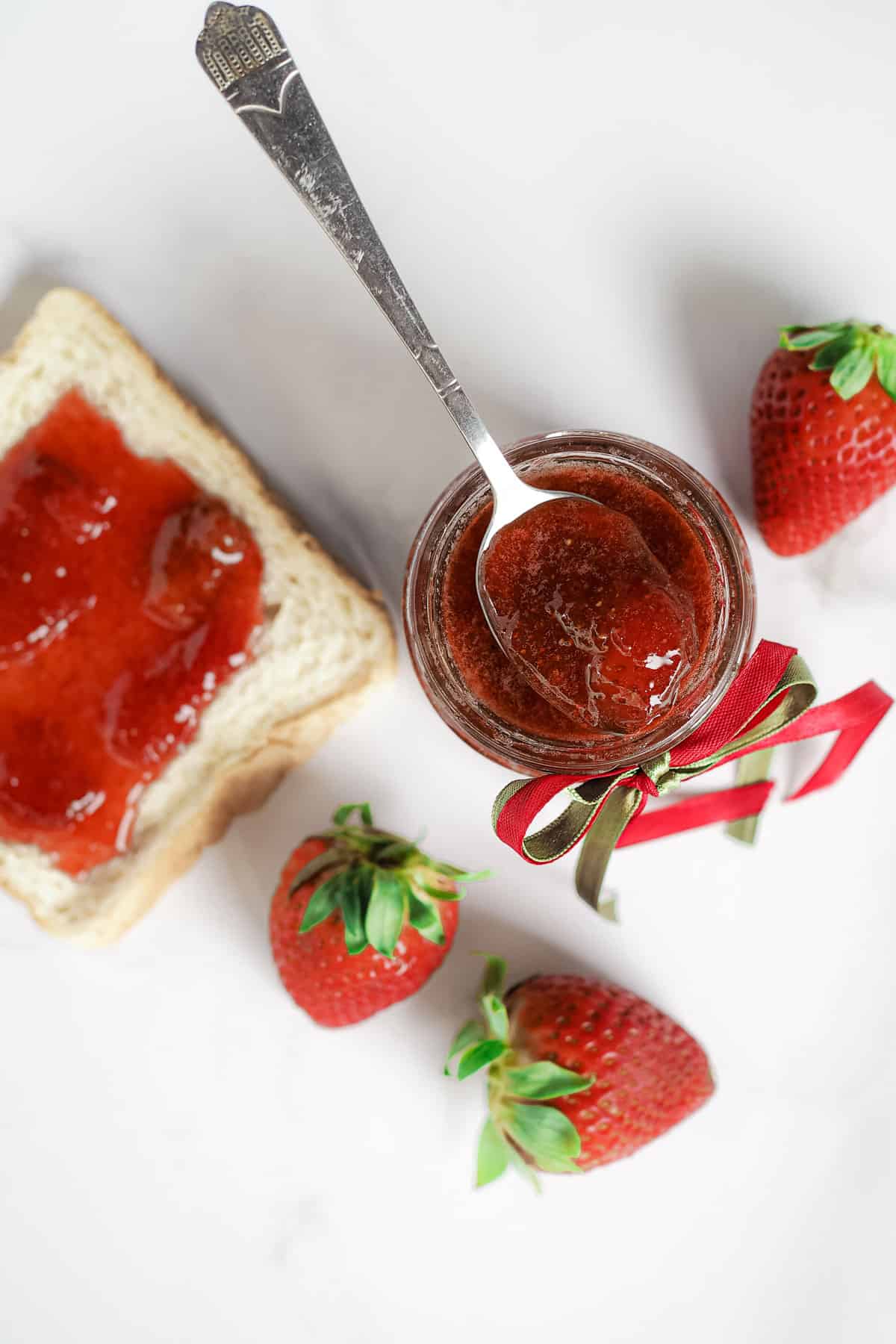 A bottle of strawberry jam with a slice of toast (with jam on) on the side.